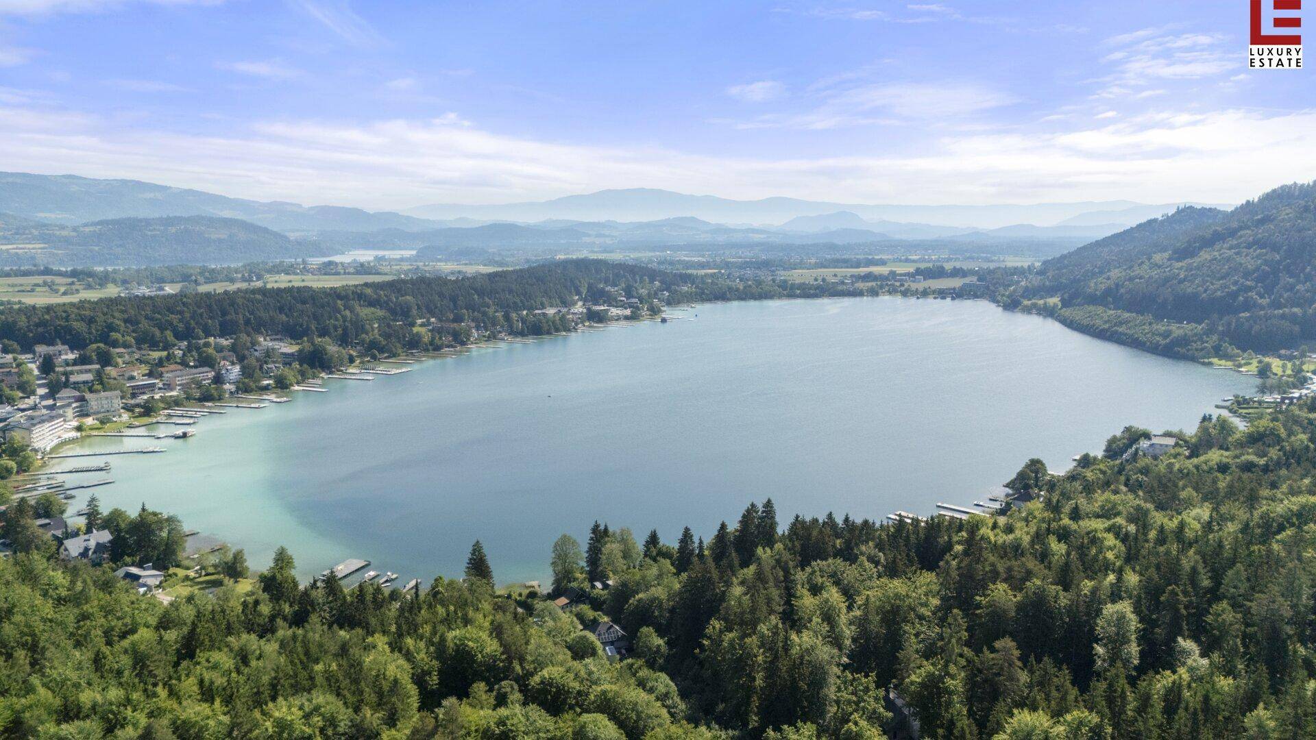 Panoramablick auf einen großen See, umgeben von dichten Wäldern und vereinzelten Häusern am Ufer.