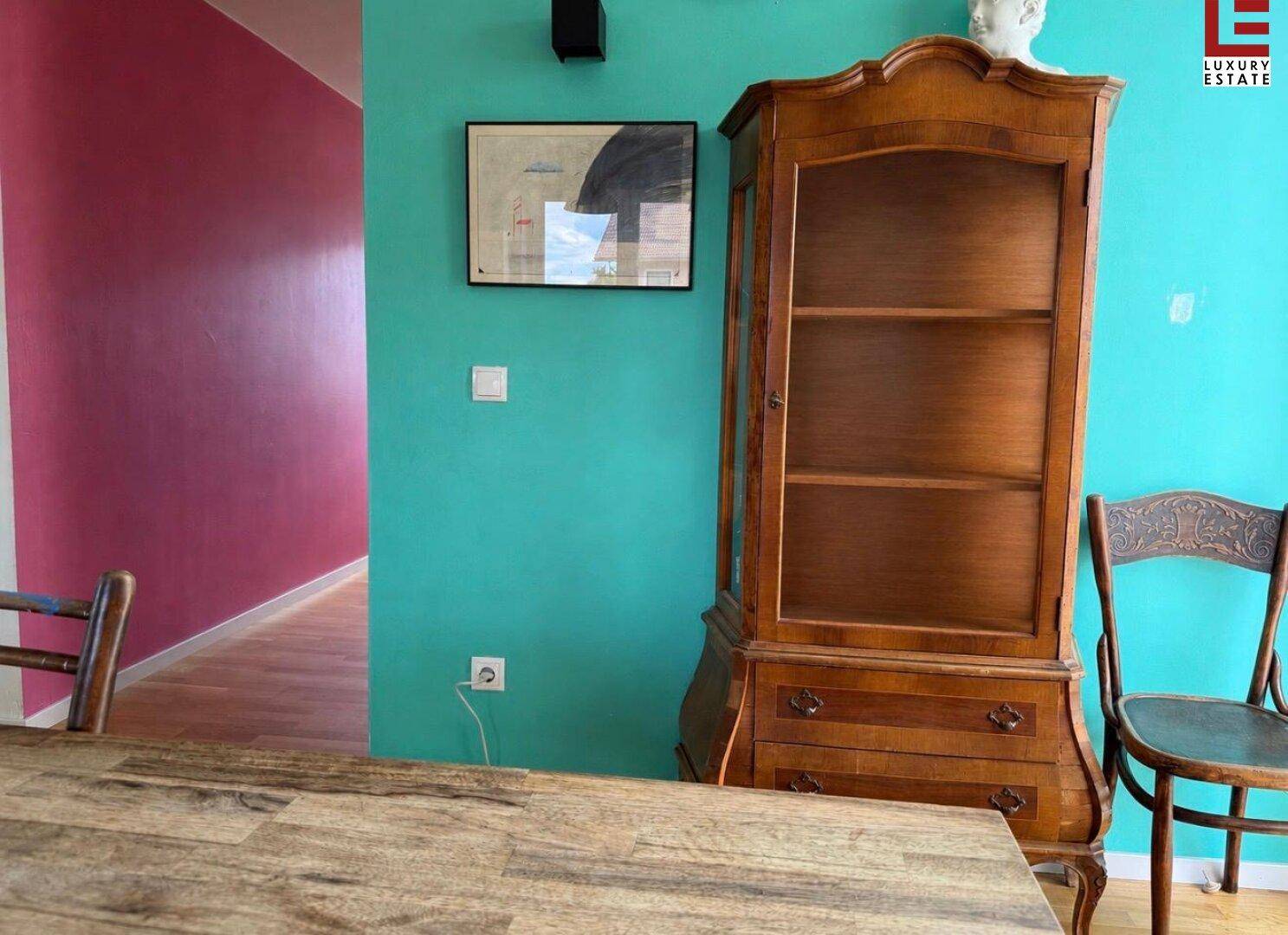 Essbereich mit antikem Holzschrank und farbigen Wänden in Türkis und Magenta.