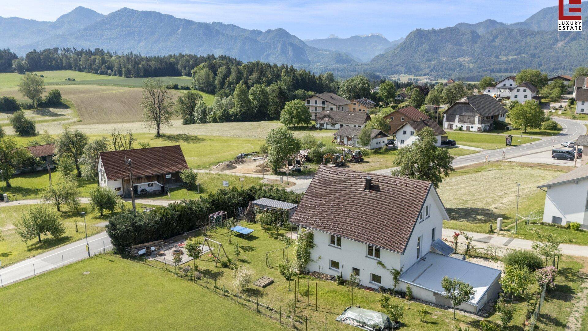 Luftaufnahme des Hauses mit Garten und der umliegenden ländlichen Siedlung und Bergen.
