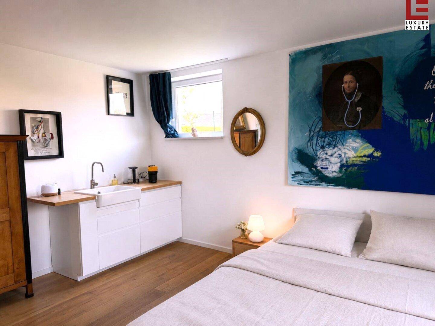 Gemütliches Schlafzimmer mit Doppelbett, kleiner Küchenzeile und farbenfrohem Kunstwerk.