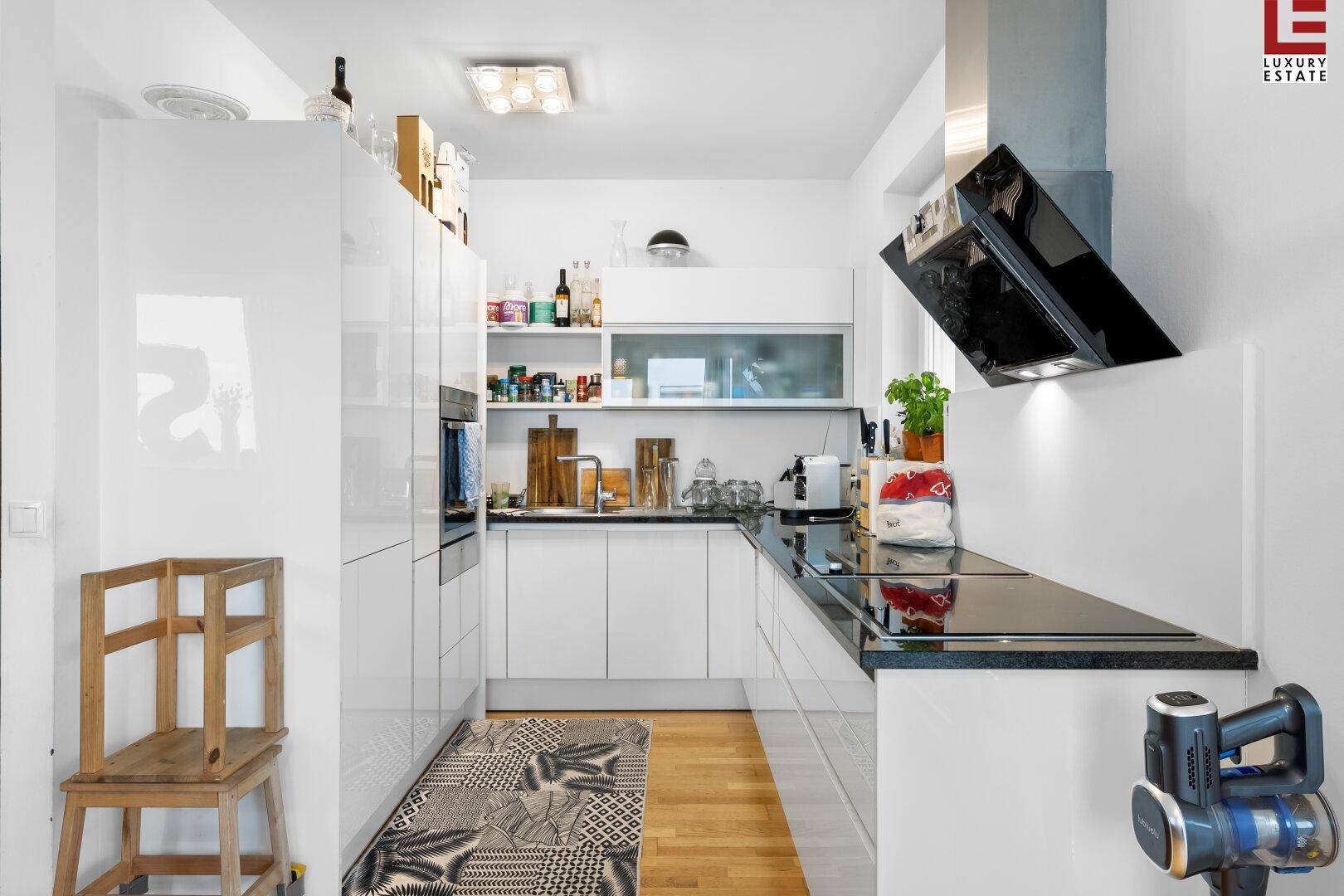 Moderne Küche mit weißen Hochglanzfronten, schwarzen Arbeitsplatten und integrierten Geräten.