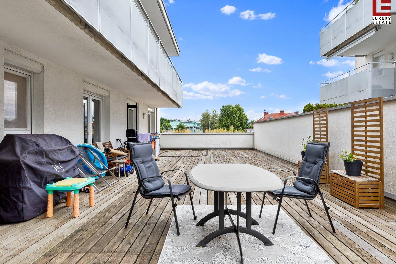 Geräumige Holzterrasse mit Sitzgelegenheiten und Grillbereich unter blauem Himmel.