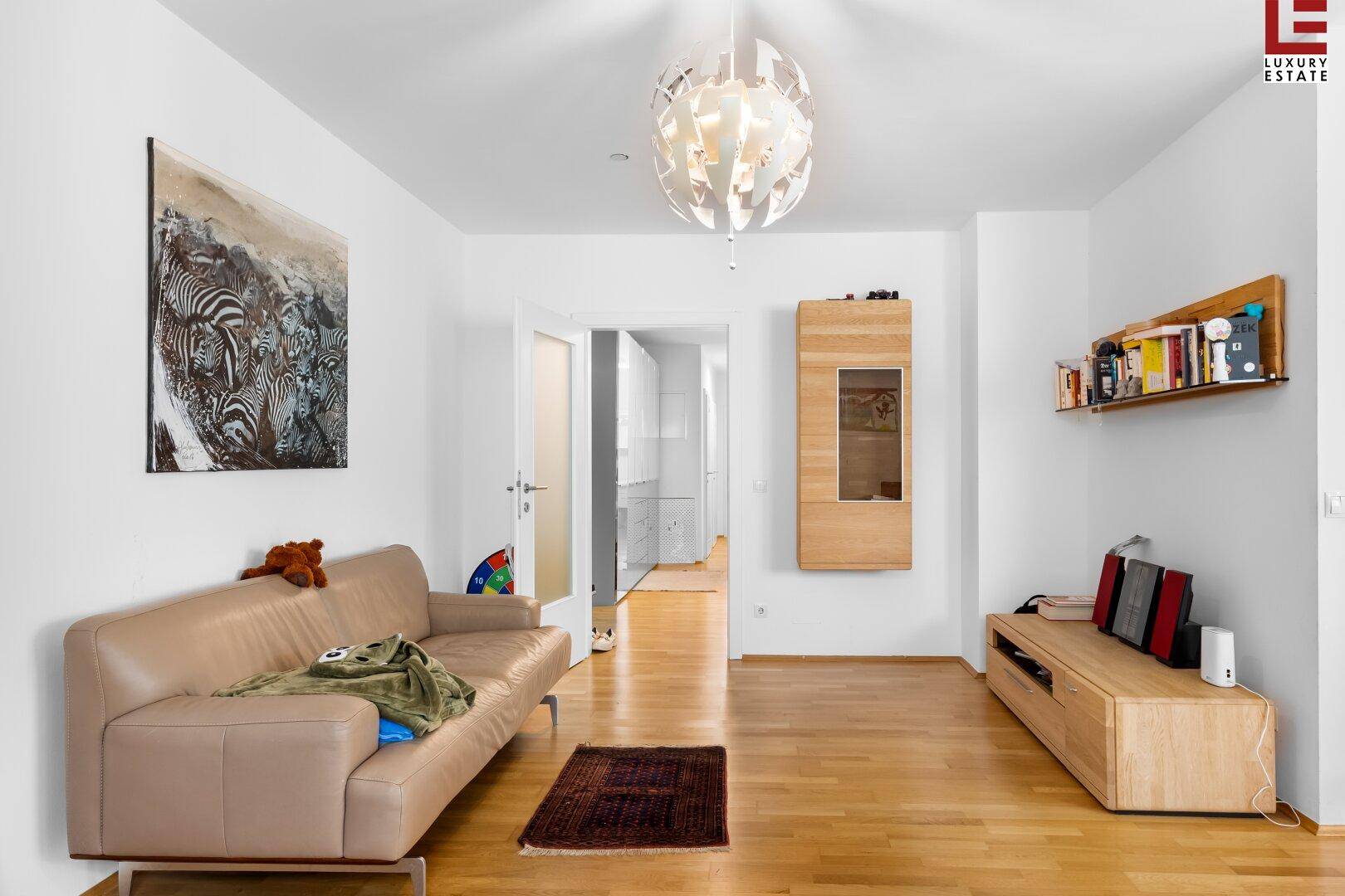 Gemütliches Wohnzimmer mit beiger Couch, Holzelementen und Zugang zu weiteren Räumen.