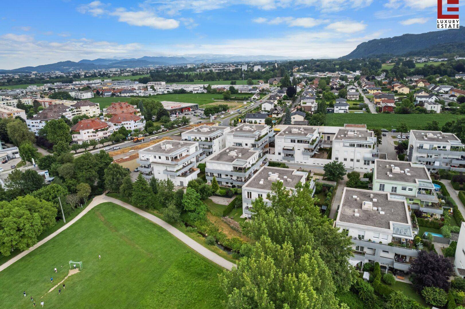 Luftaufnahme einer modernen Wohnsiedlung mit Grünflächen und Bergblick in der Ferne.