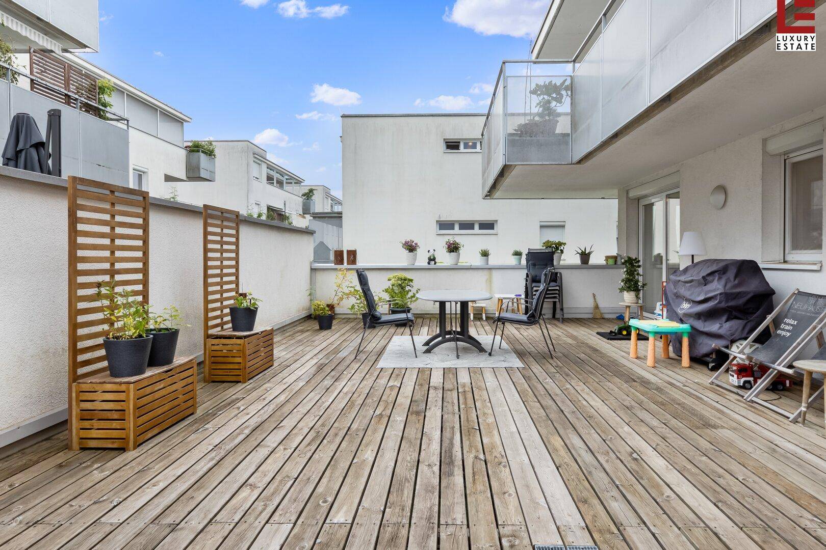 Weitläufige Holzterrasse mit Blick auf die moderne Gebäudefassade und den blauen Himmel.