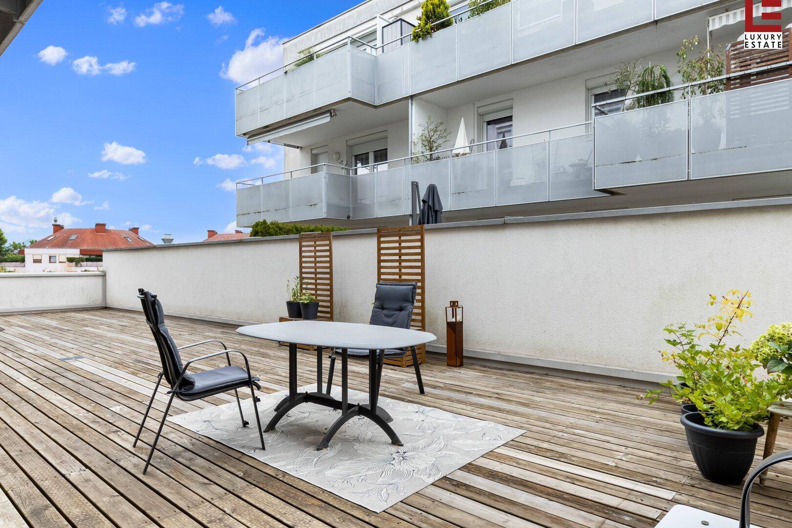 Detailansicht der Holzterrasse mit Esstisch und Stühlen, umgeben von Pflanzen.