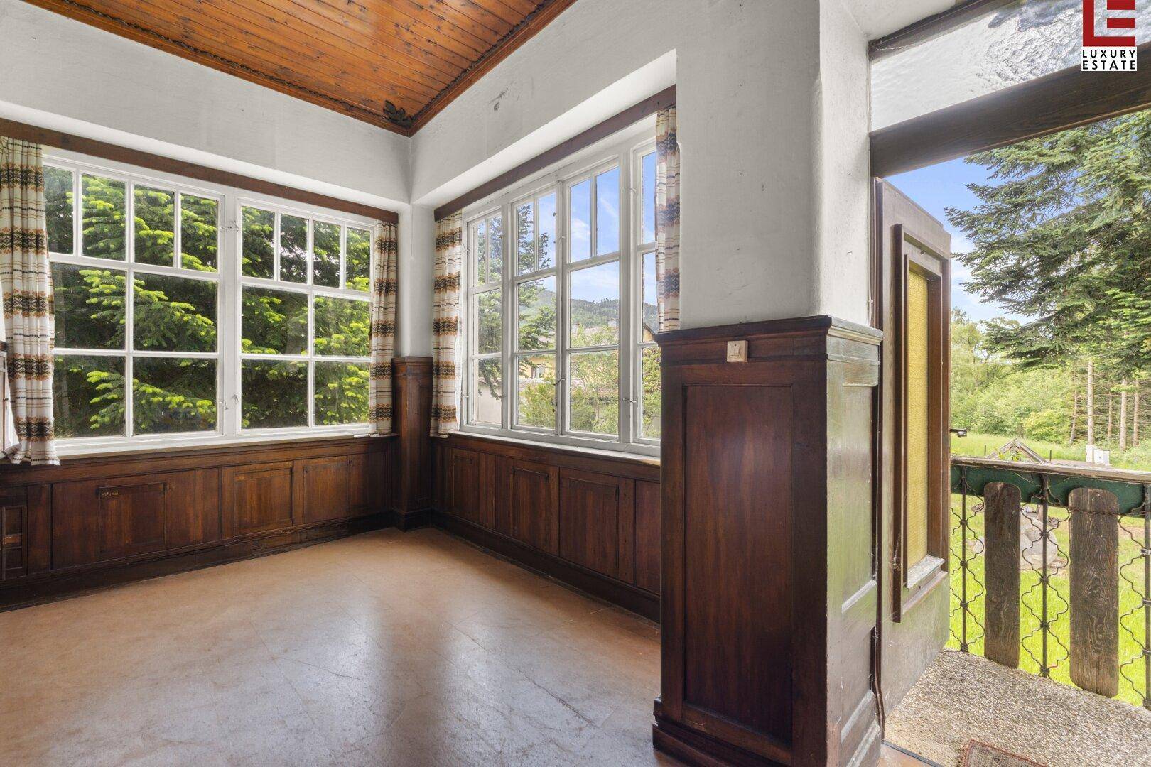 Heller Innenraum mit vielen Fenstern, Holzvertäfelung und Holzbalkendecke.