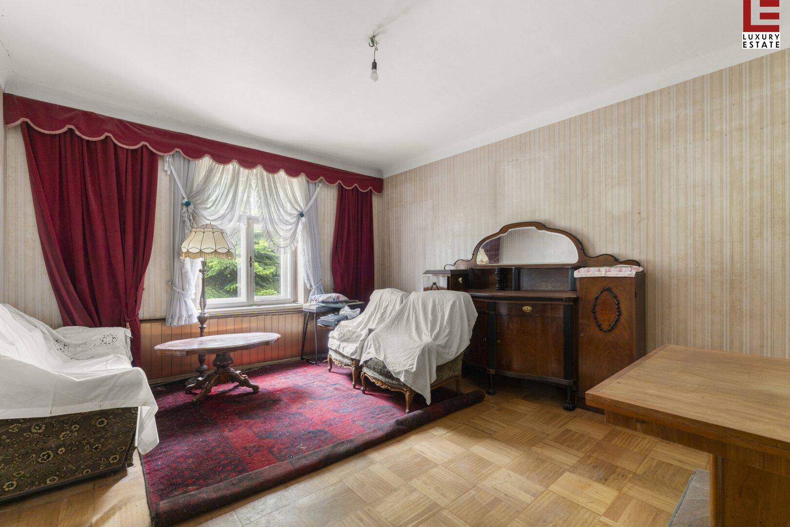 Traditionelles Wohnzimmer mit Parkettboden, gemusterter Tapete und antiken Möbeln.