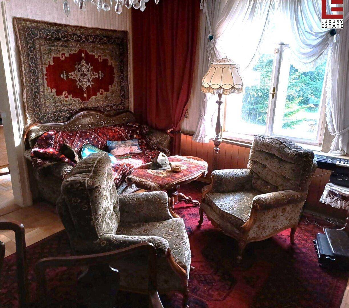 Gemütliches Wohnzimmer mit antiken Sesseln, Teppich und einem großen Fenster mit Vorhängen.
