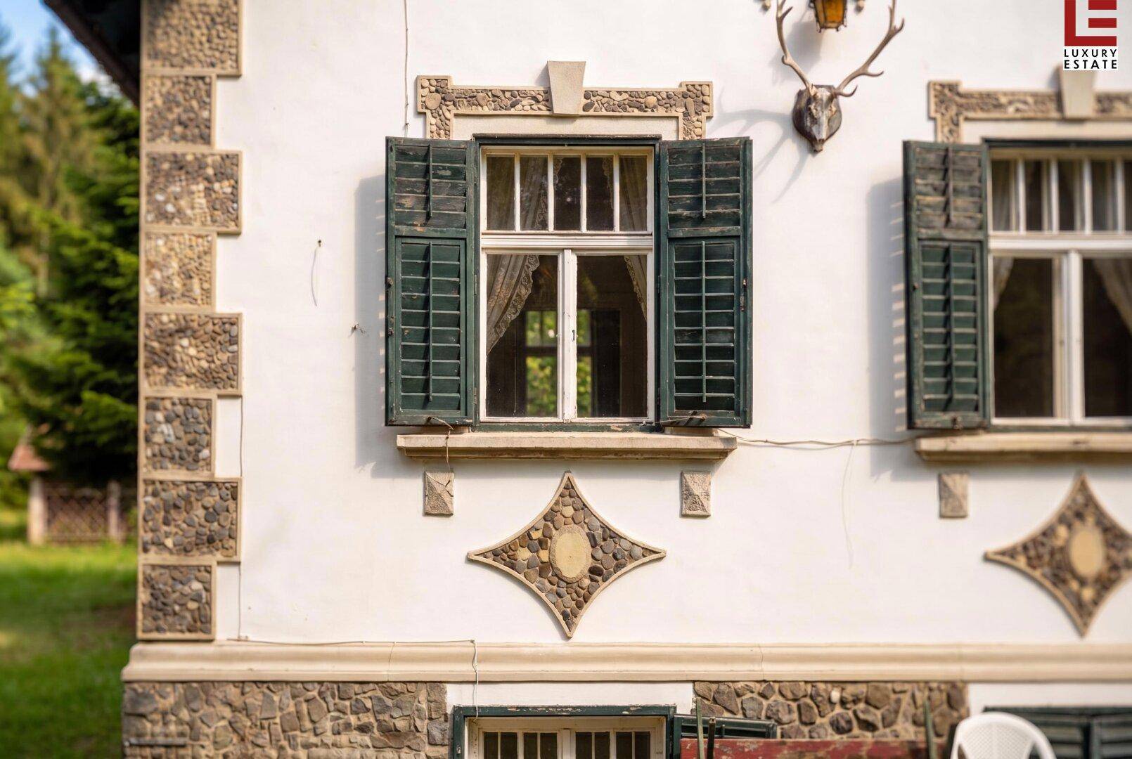 Detailansicht der Hausfassade mit grünen Fensterläden, Steinelementen und Hirschgeweih.