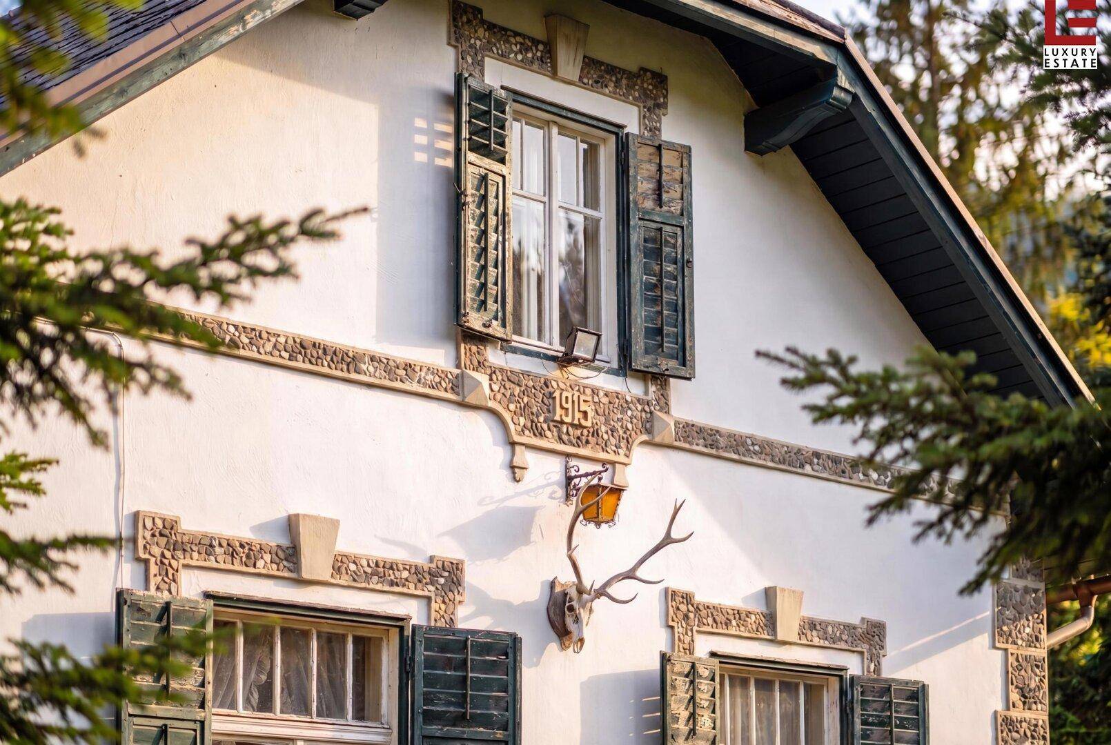 Detailansicht der Hausfassade mit Jahreszahl 1915, Hirschgeweih und dekorativen Elementen.