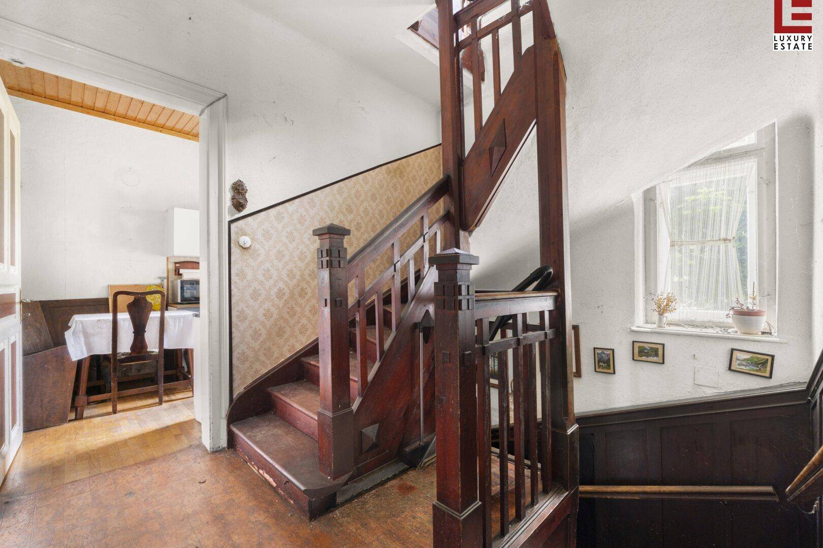 Historisches Treppenhaus mit Holzgeländer, gemusterter Tapete und Fenster.