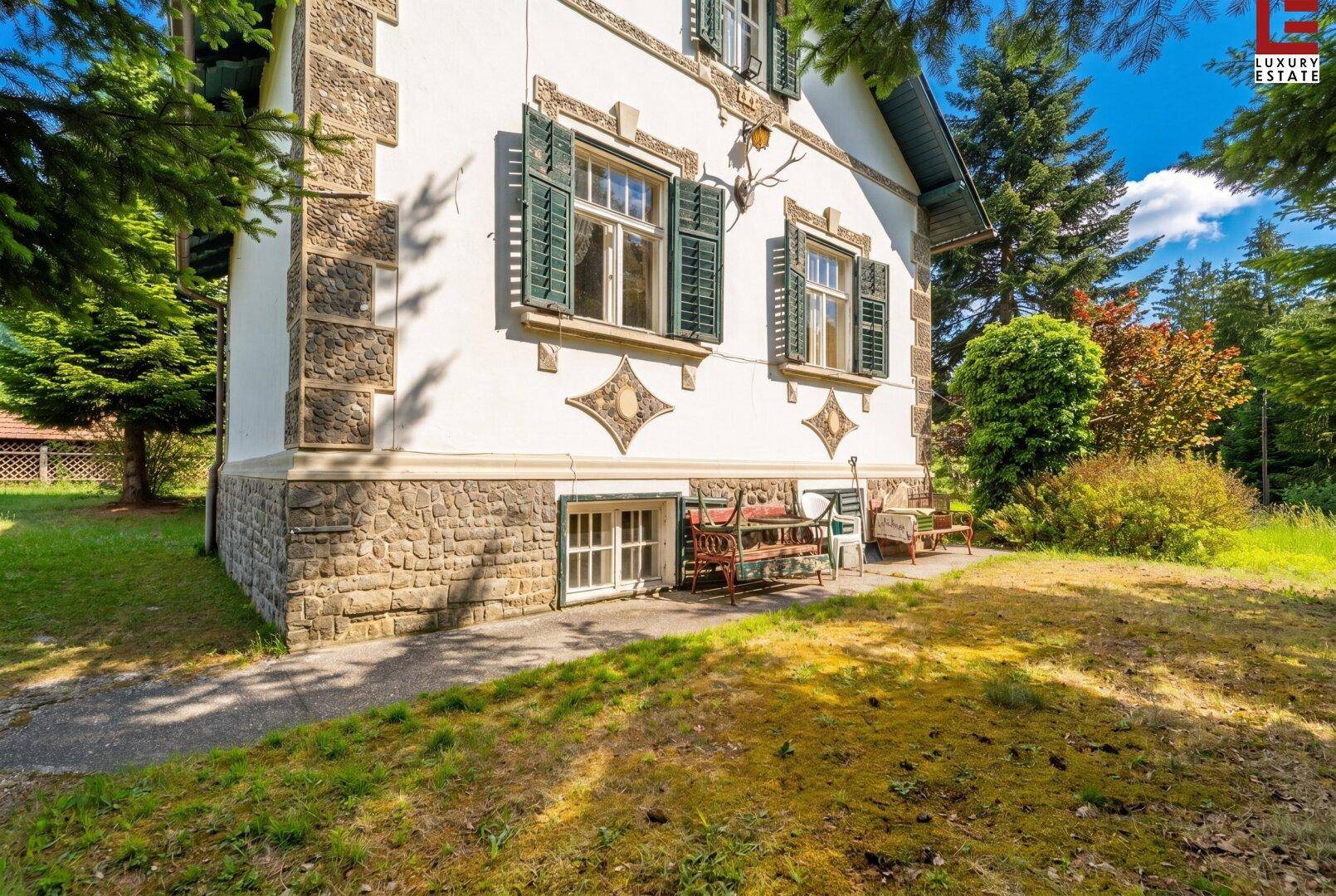 Seitenansicht des Hauses mit Steinfassade, grünen Fensterläden und Gartenbereich.
