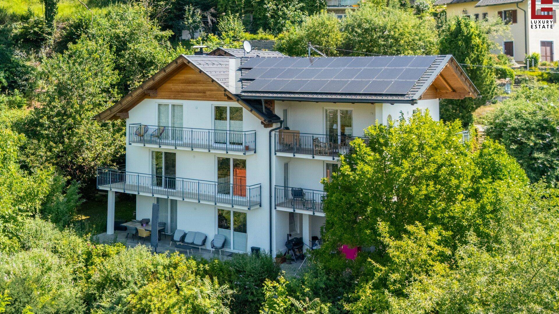 Attraktives Wohnhaus mit mehreren Balkonen und Solarpaneelen auf dem Dach, umgeben von Bäumen.