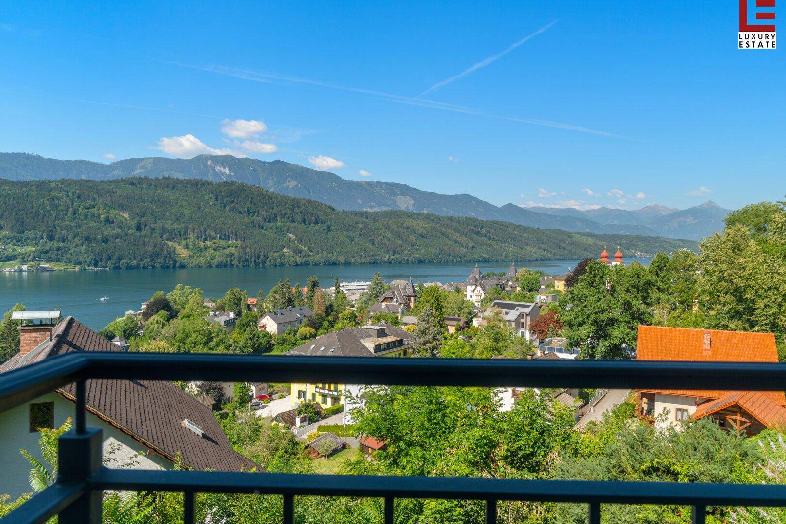 Panoramablick vom Balkon auf den glitzernden See, die umliegende Stadt und die majestätischen Berge.