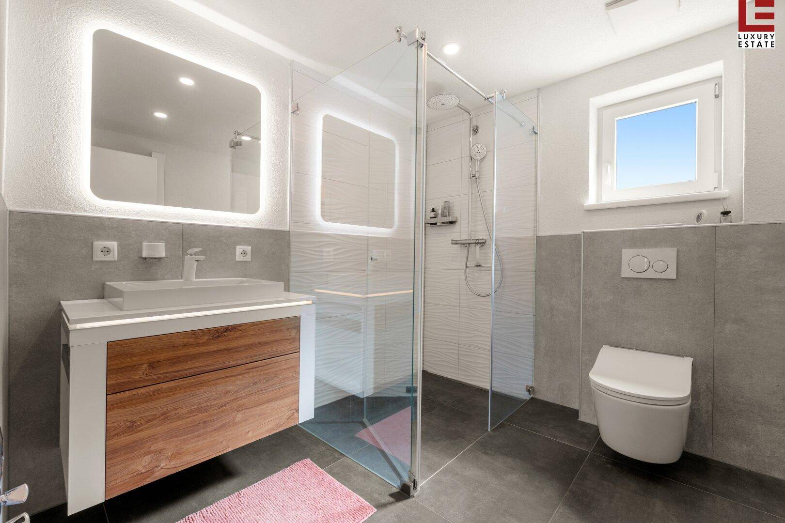 Modernes Badezimmer mit begehbarer Dusche, eleganten Fliesen und beleuchtetem Spiegel.