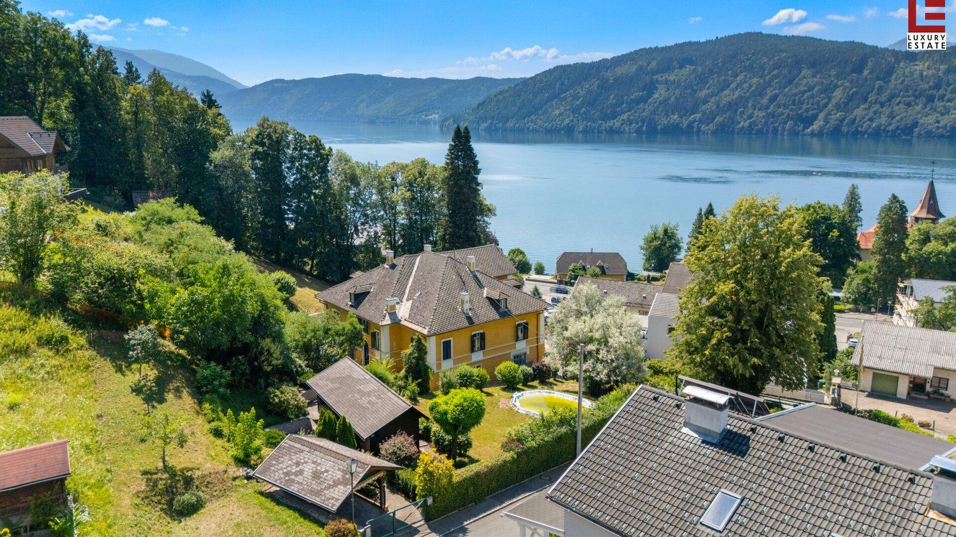 Malerische Luftaufnahme eines Anwesens am See mit umliegender Natur und Bergen im Hintergrund.