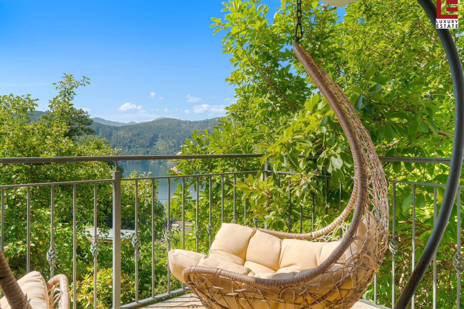 Gemütlicher Hängesessel auf dem Balkon mit weitem Blick auf den See und die umliegende Berglandschaft.