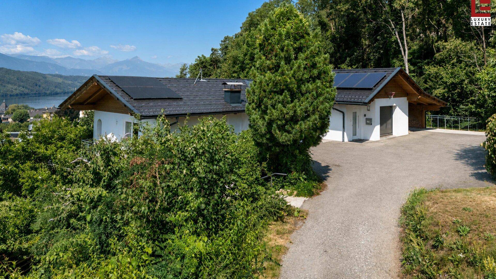 Modernes Wohnhaus mit Photovoltaikanlage und Zufahrt, umgeben von grüner Natur und Bäumen.