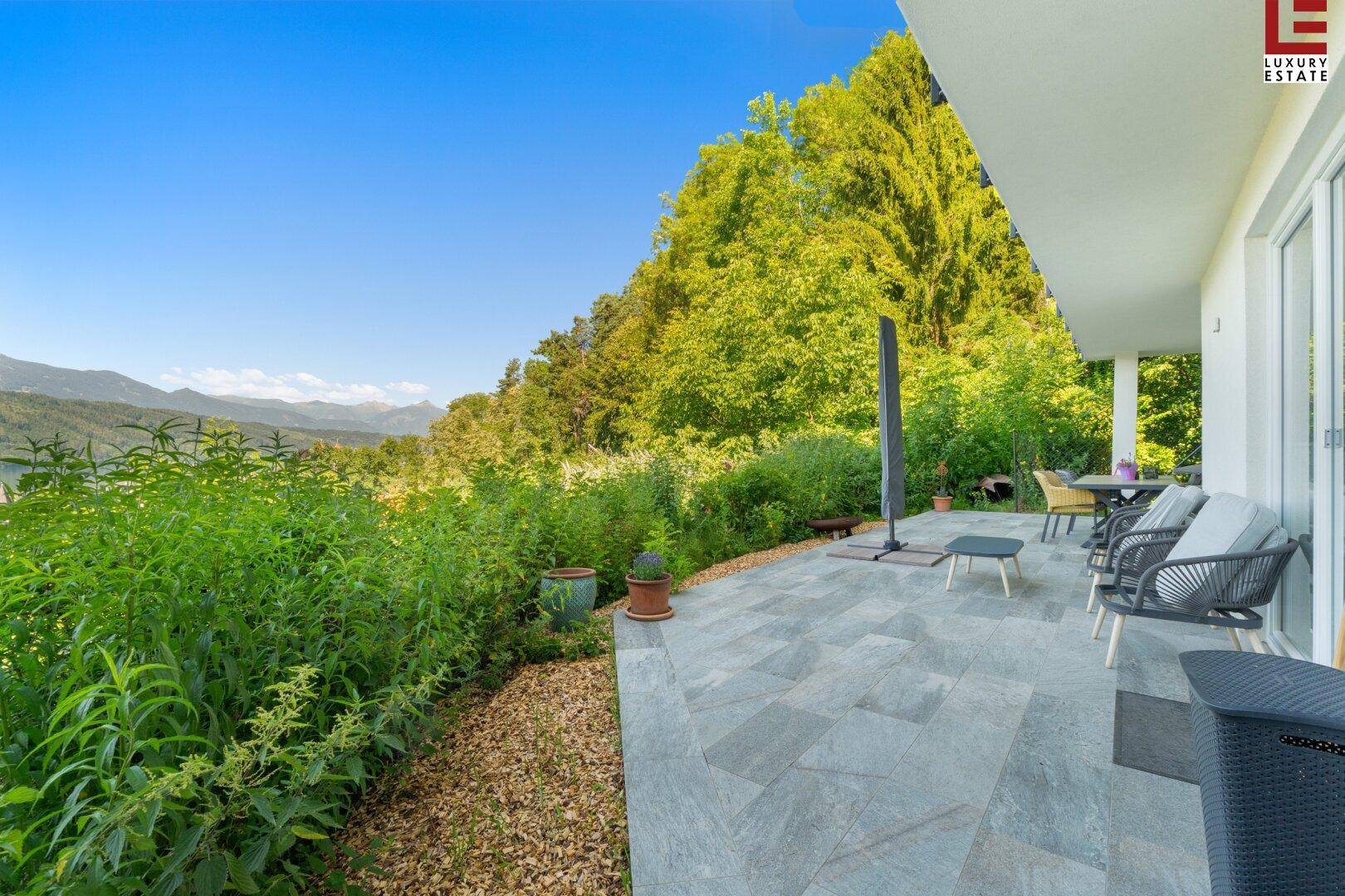 Große geflieste Terrasse mit Gartenmöbeln und weitem Blick auf die umliegende Natur und Berge.
