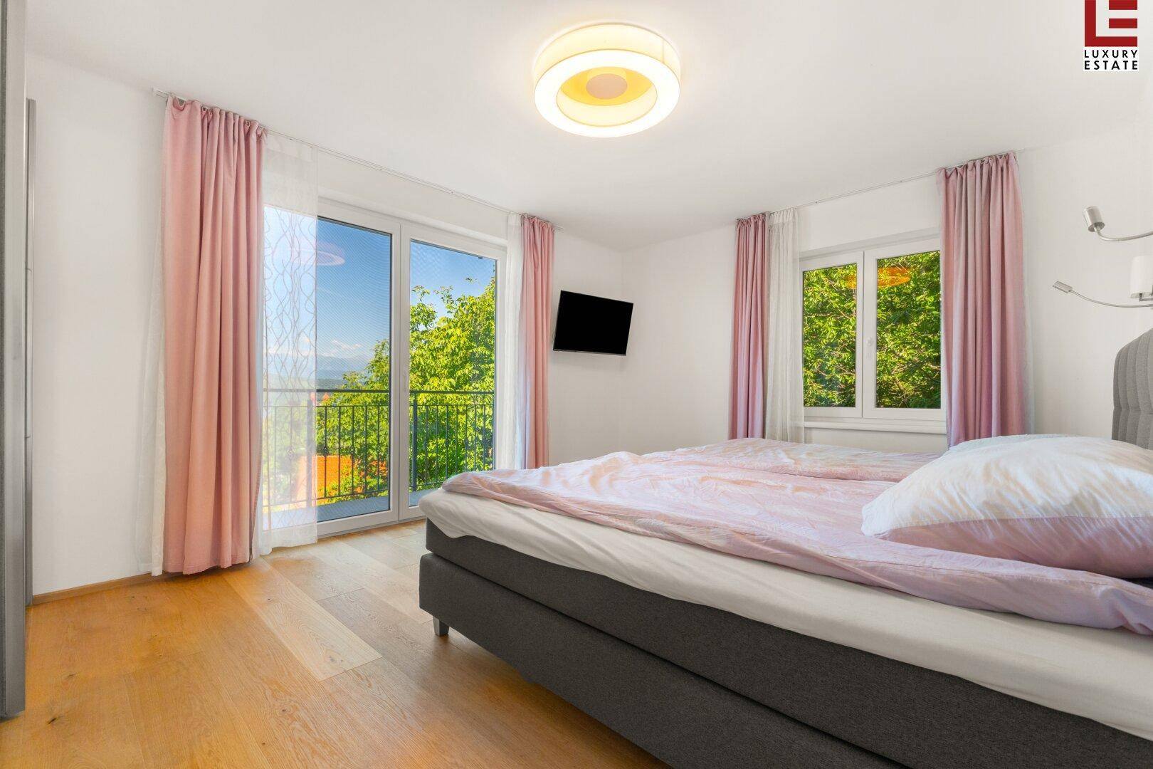 Gemütliches Schlafzimmer mit Holzboden, Zugang zum Balkon und Blick auf die grüne Umgebung.