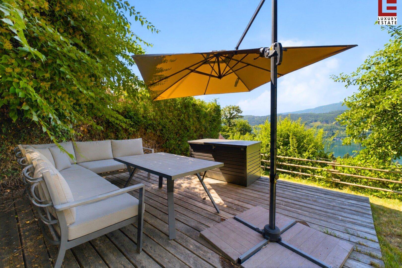 Holzterrasse mit bequemen Gartenmöbeln und Sonnenschirm, bietet einen schönen Blick auf den See.