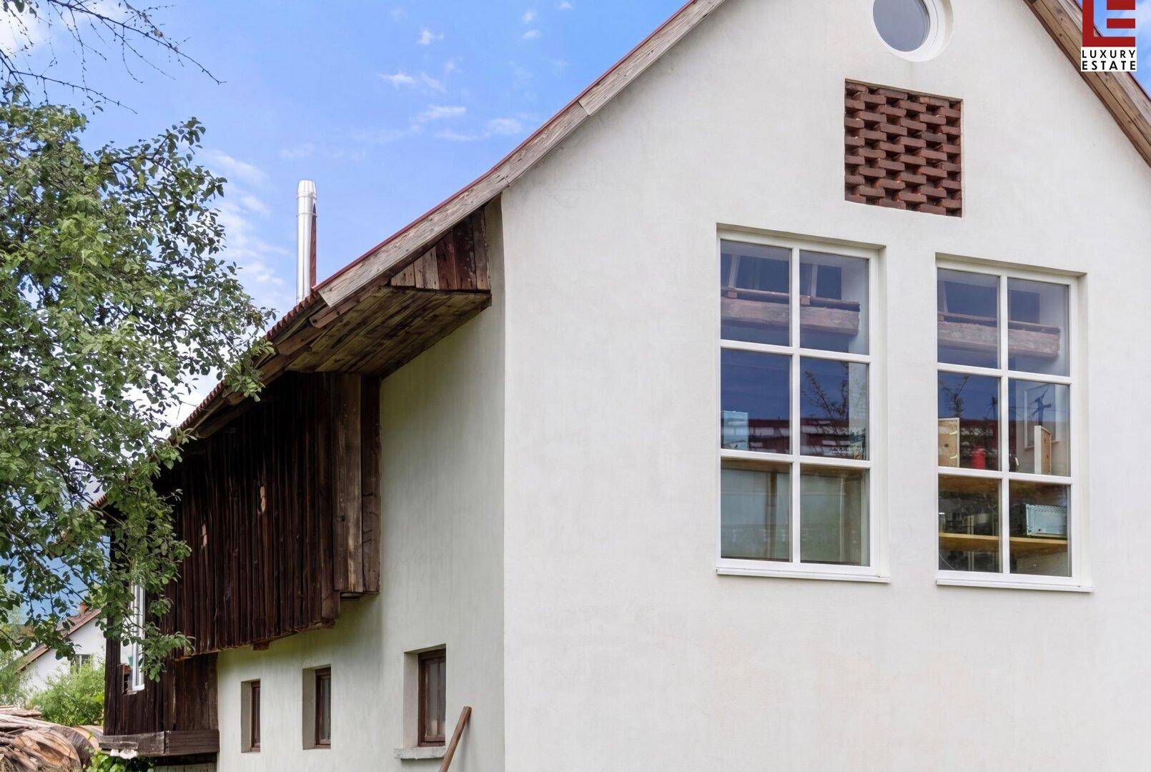 Seitenansicht des Gebäudes mit weißer Fassade, Holzverkleidung und mehreren Fenstern.