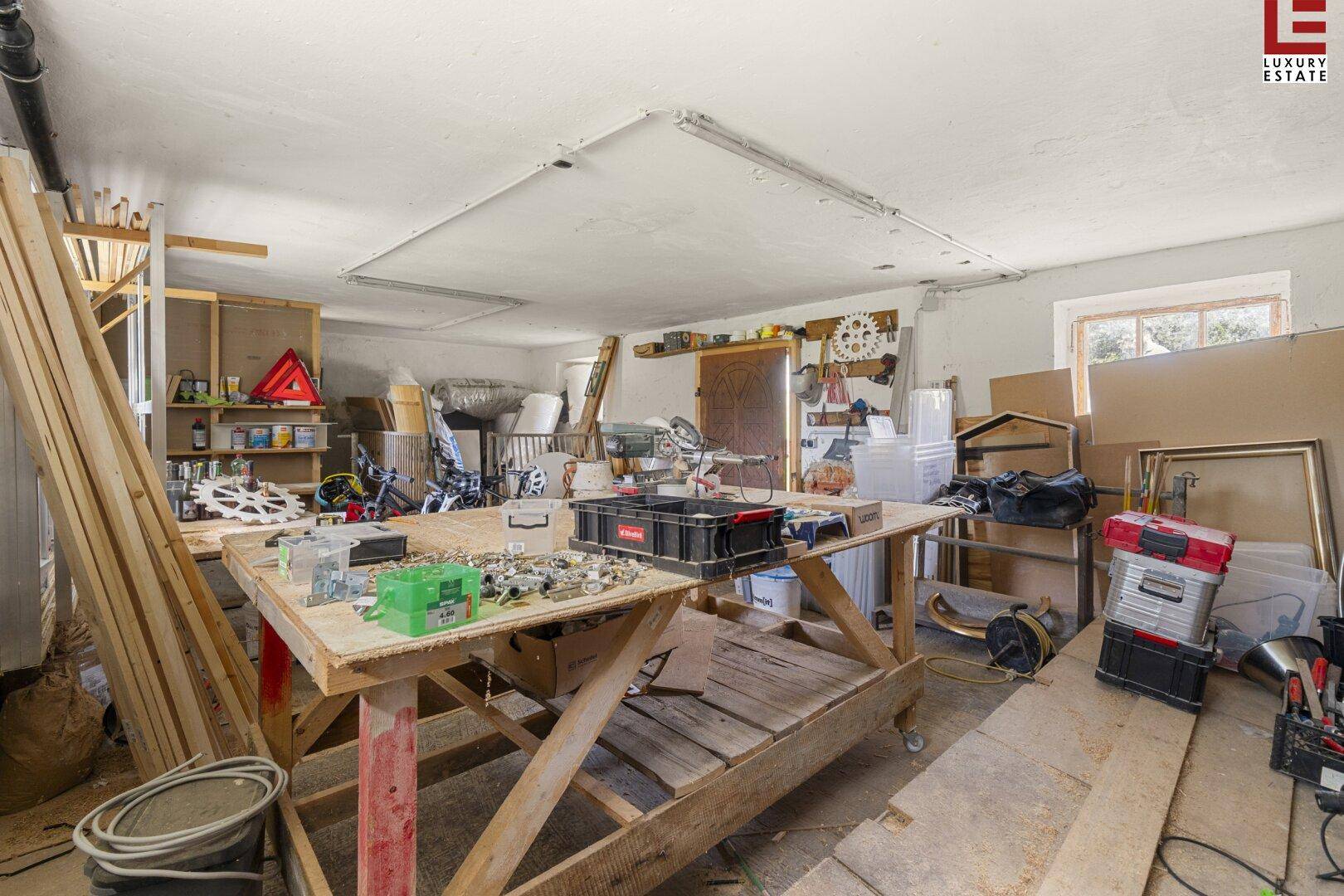 Geräumiger Werkstattraum mit Arbeitstischen, Regalen und verschiedenen Werkzeugen und Materialien.