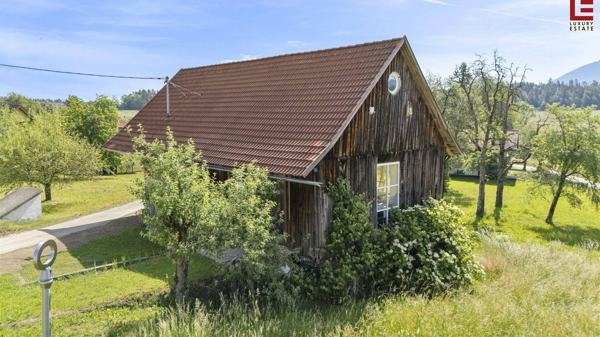 Ländliches Gebäude mit Holzfassade und Ziegeldach, umgeben von grünen Wiesen und Bäumen.