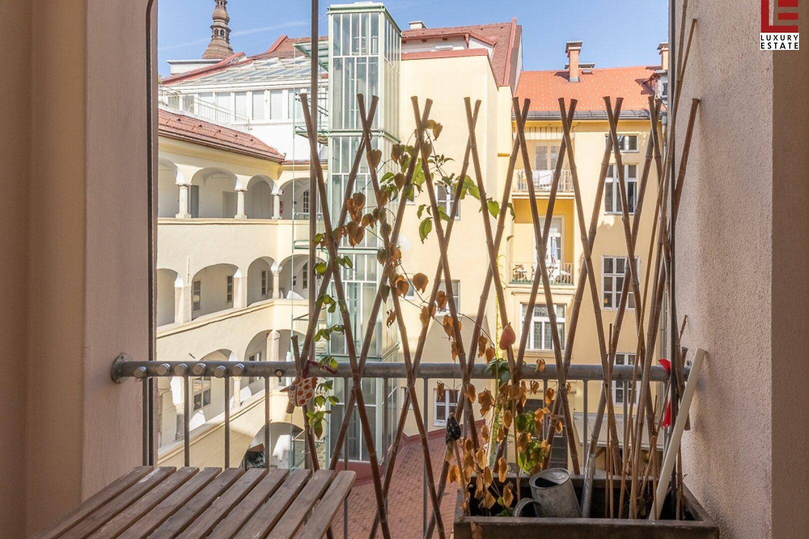 Kleiner Balkon mit Holztisch und Blick auf den Innenhof des Gebäudes.