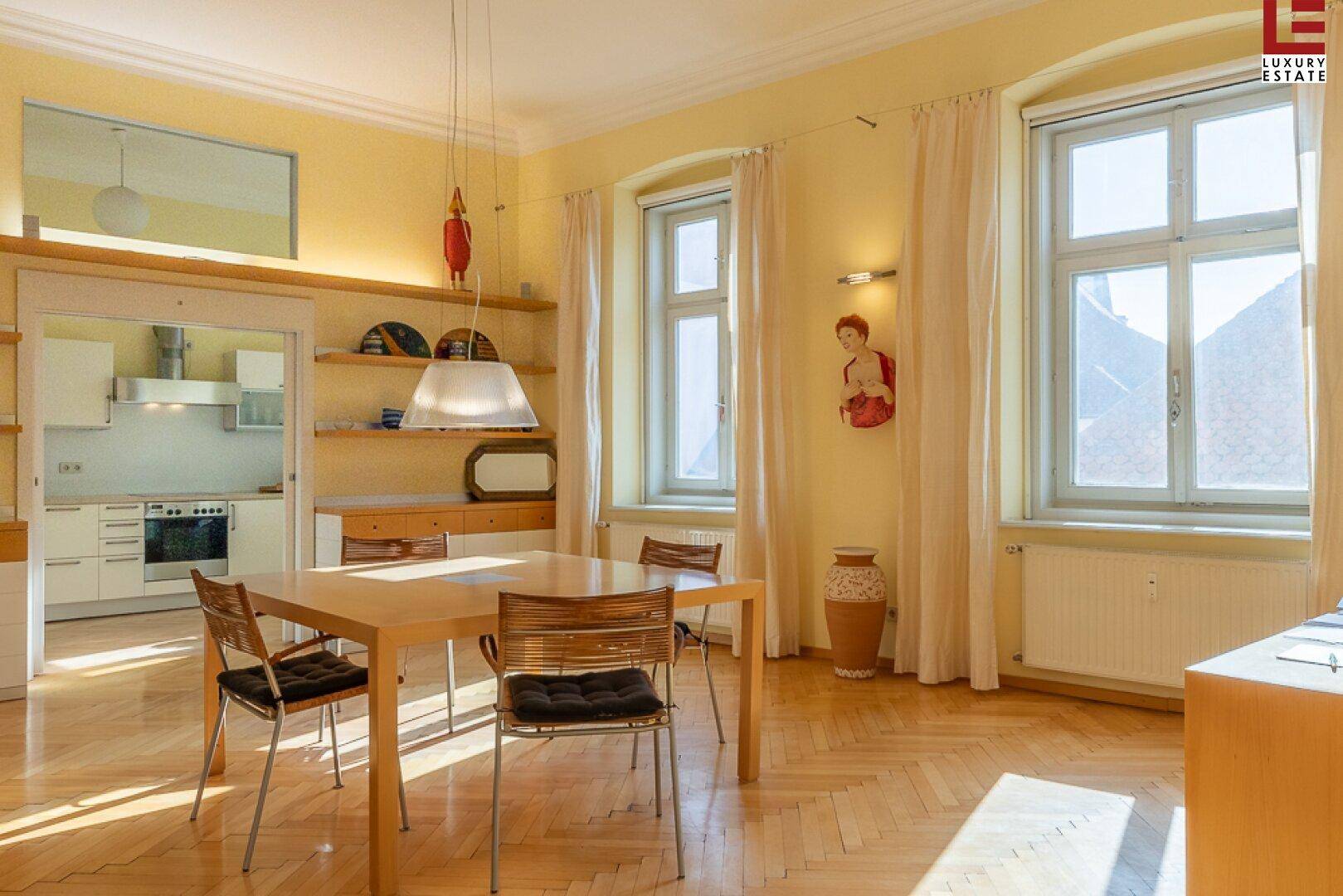 Offener Wohn- und Essbereich mit Holztisch, Parkettboden und Blick zur Küche.