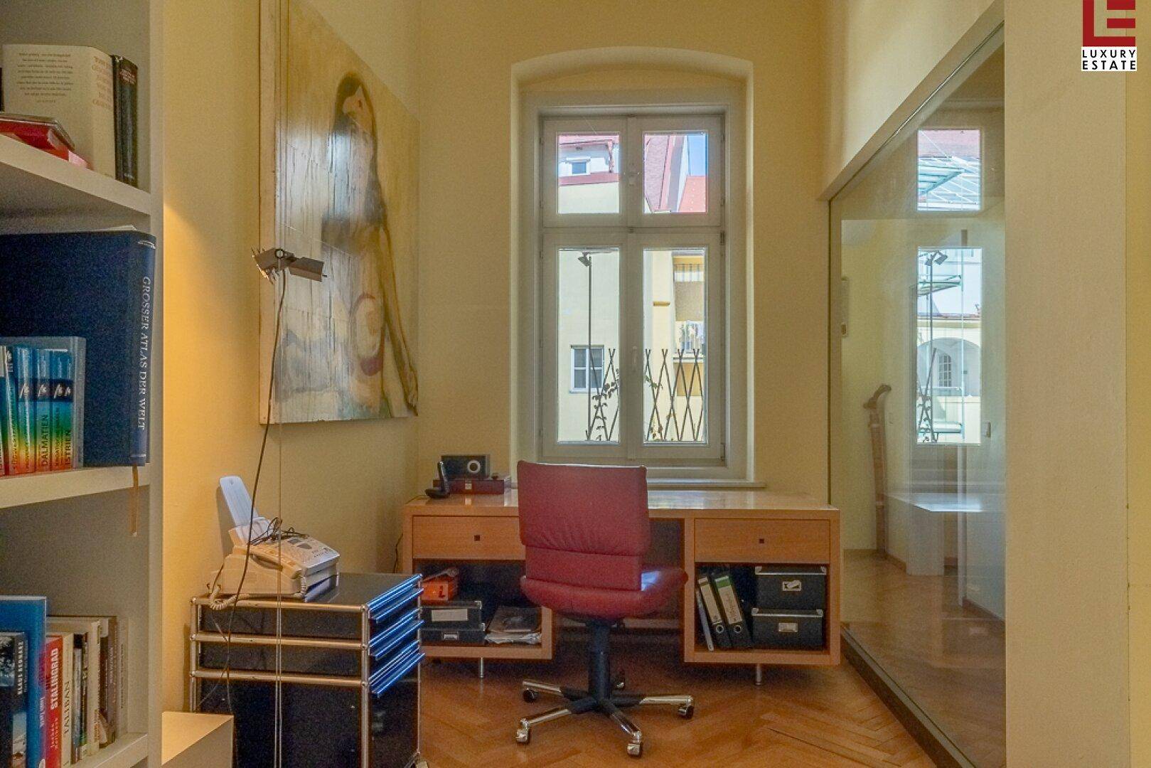 Helles Arbeitszimmer mit Schreibtisch, Bücherregal und Fenster zum Innenhof.