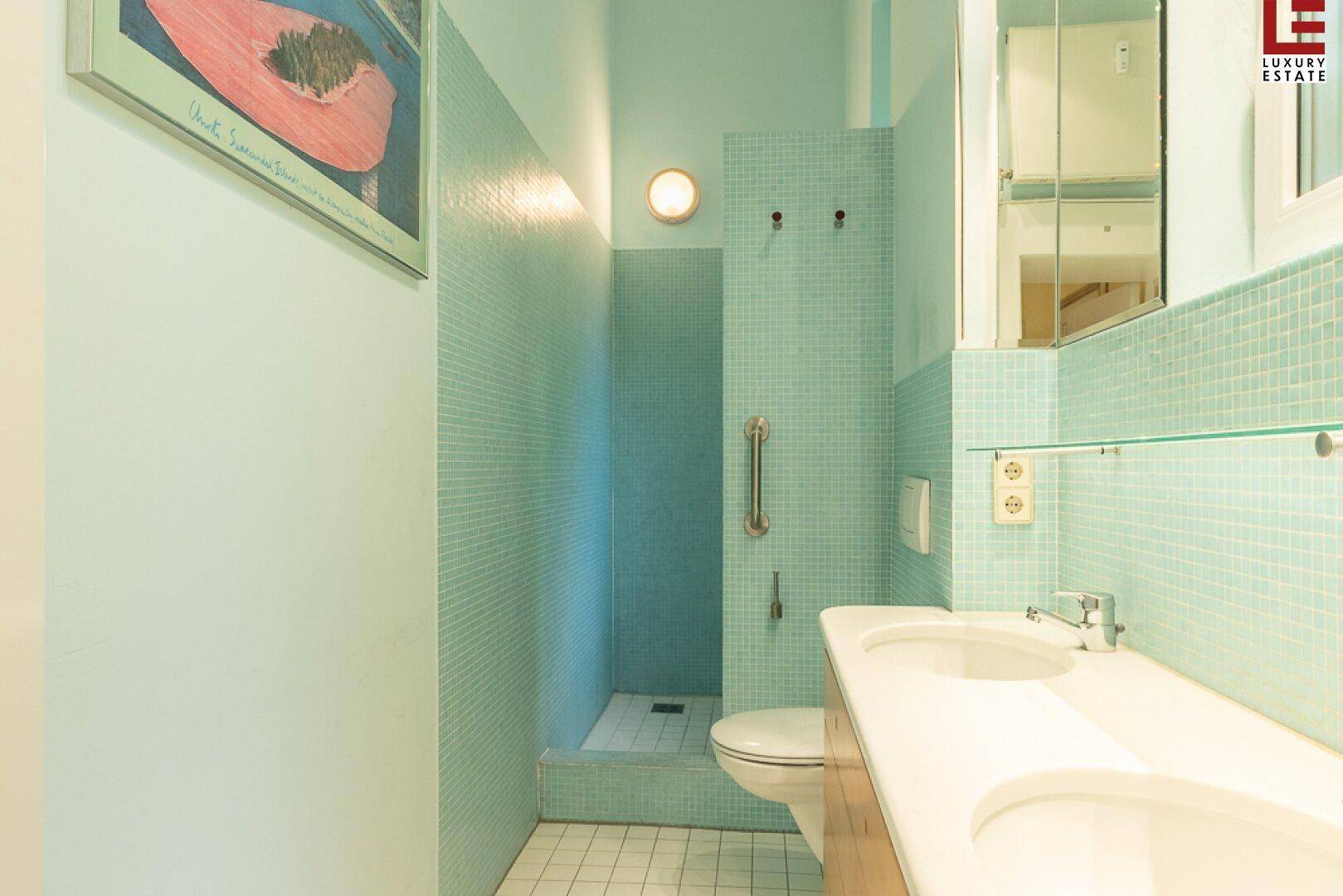 Badezimmer mit zwei Waschbecken, Dusche und hellblauen Mosaikfliesen.