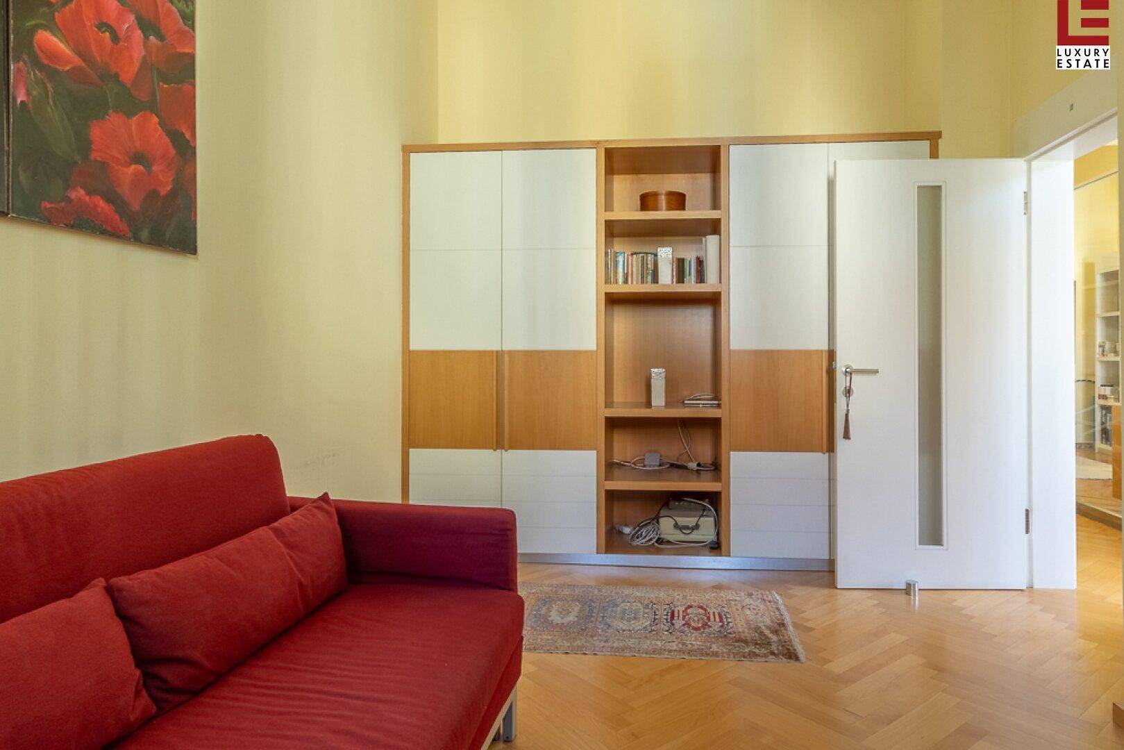Multifunktionaler Raum mit rotem Sofa, Einbauschrank und Parkettboden.