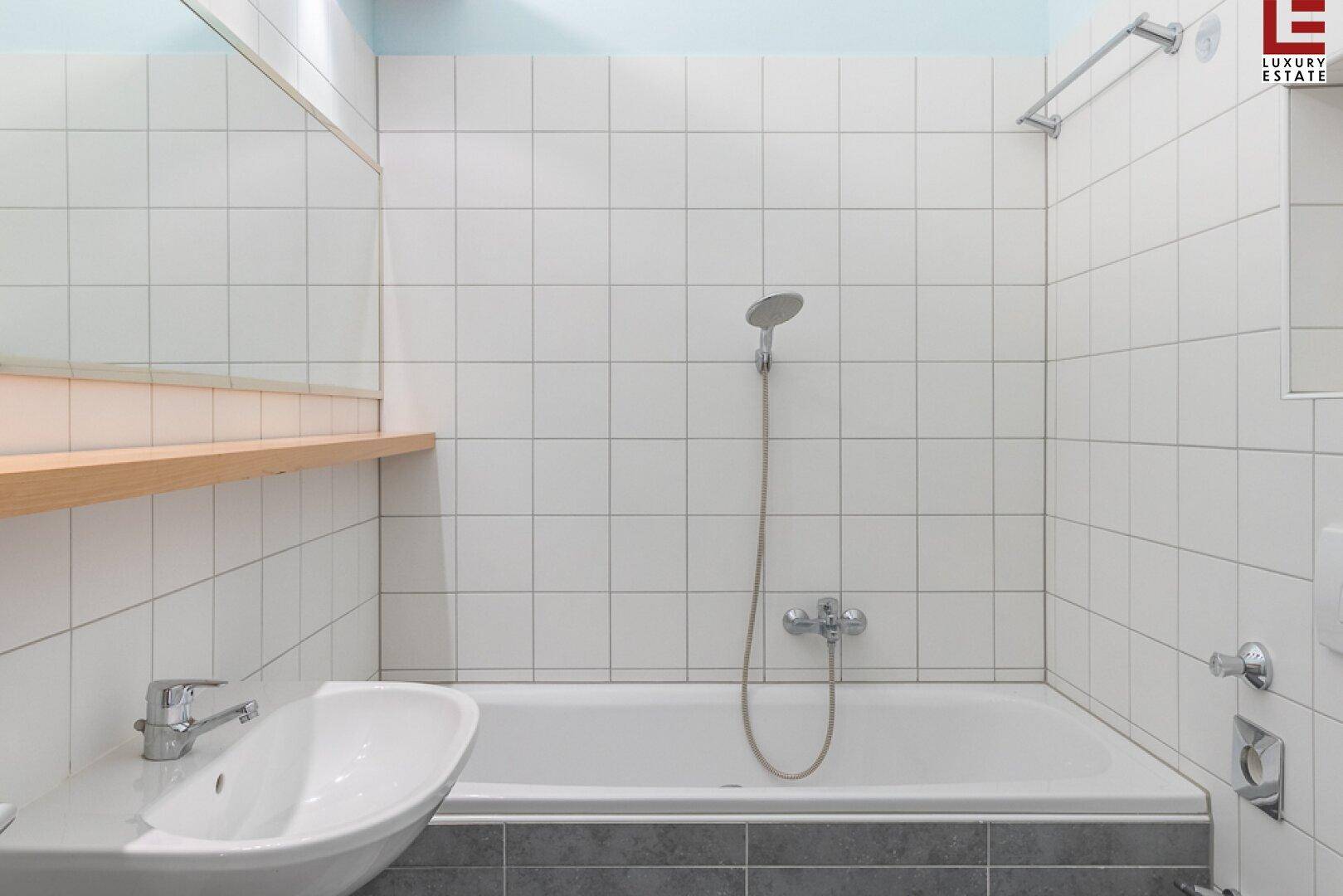Helles Badezimmer mit Badewanne, Duschkopf und weißen Wandfliesen.