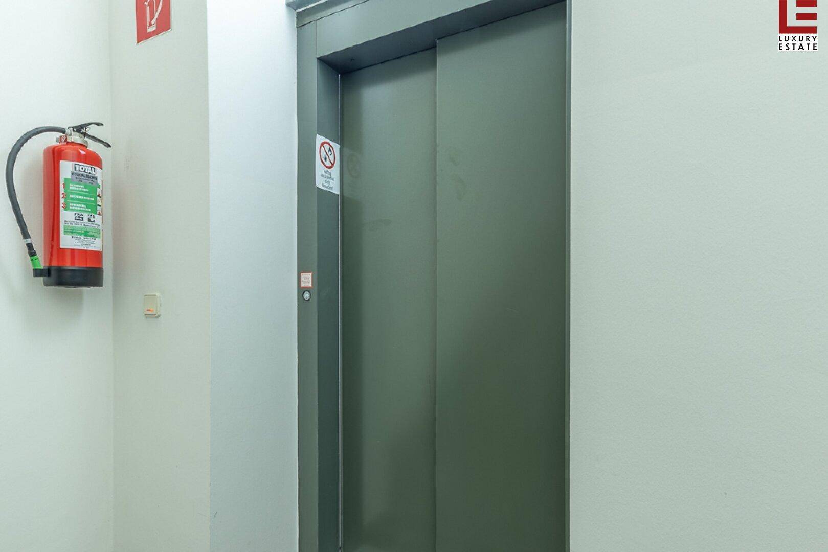 Nahaufnahme einer Aufzugstür in einem Flur, mit einem Feuerlöscher an der Wand.