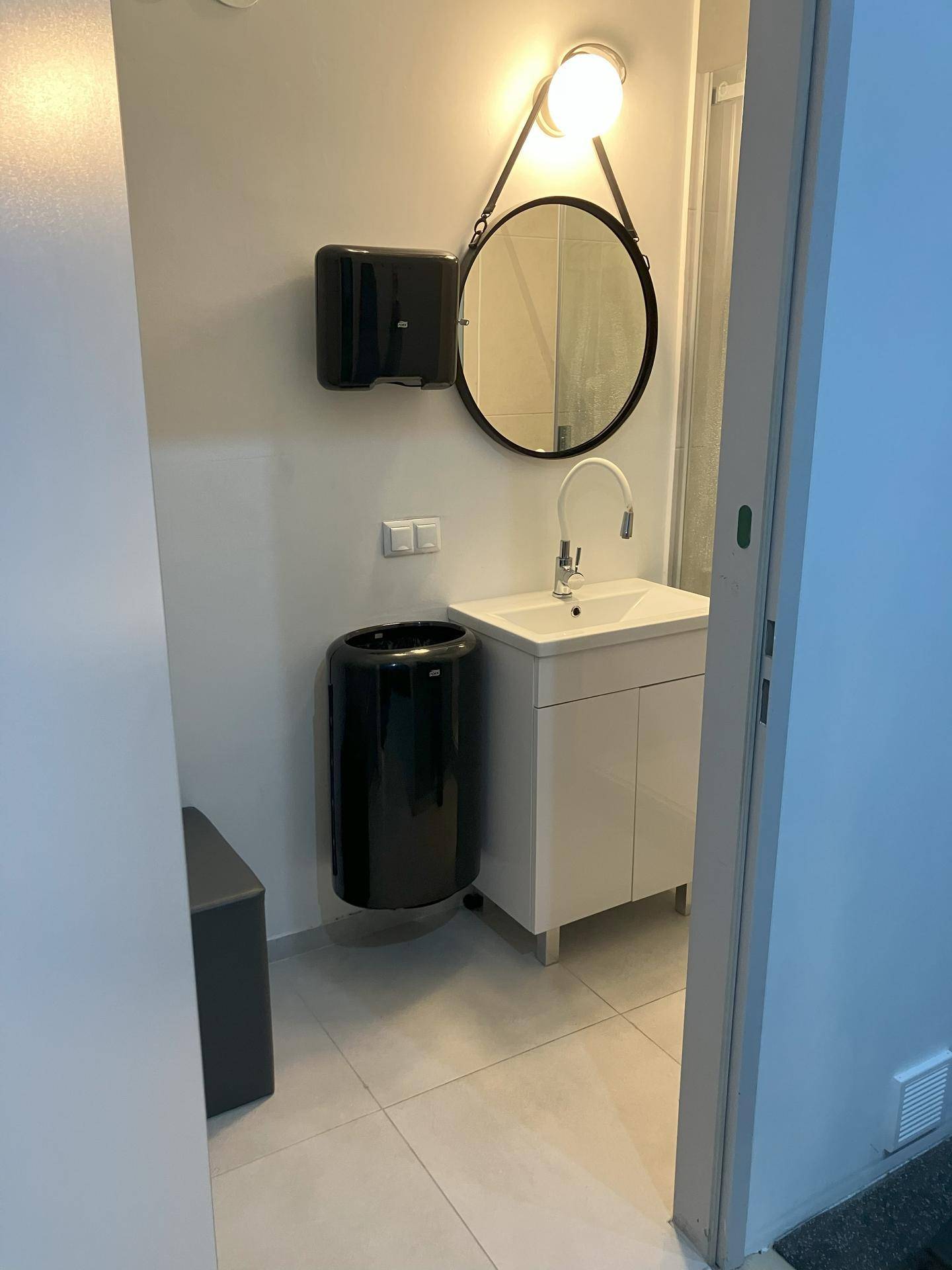 Modernes Badezimmer mit Waschbecken, rundem Spiegel und dunklen Akzenten, funktional und stilvoll.