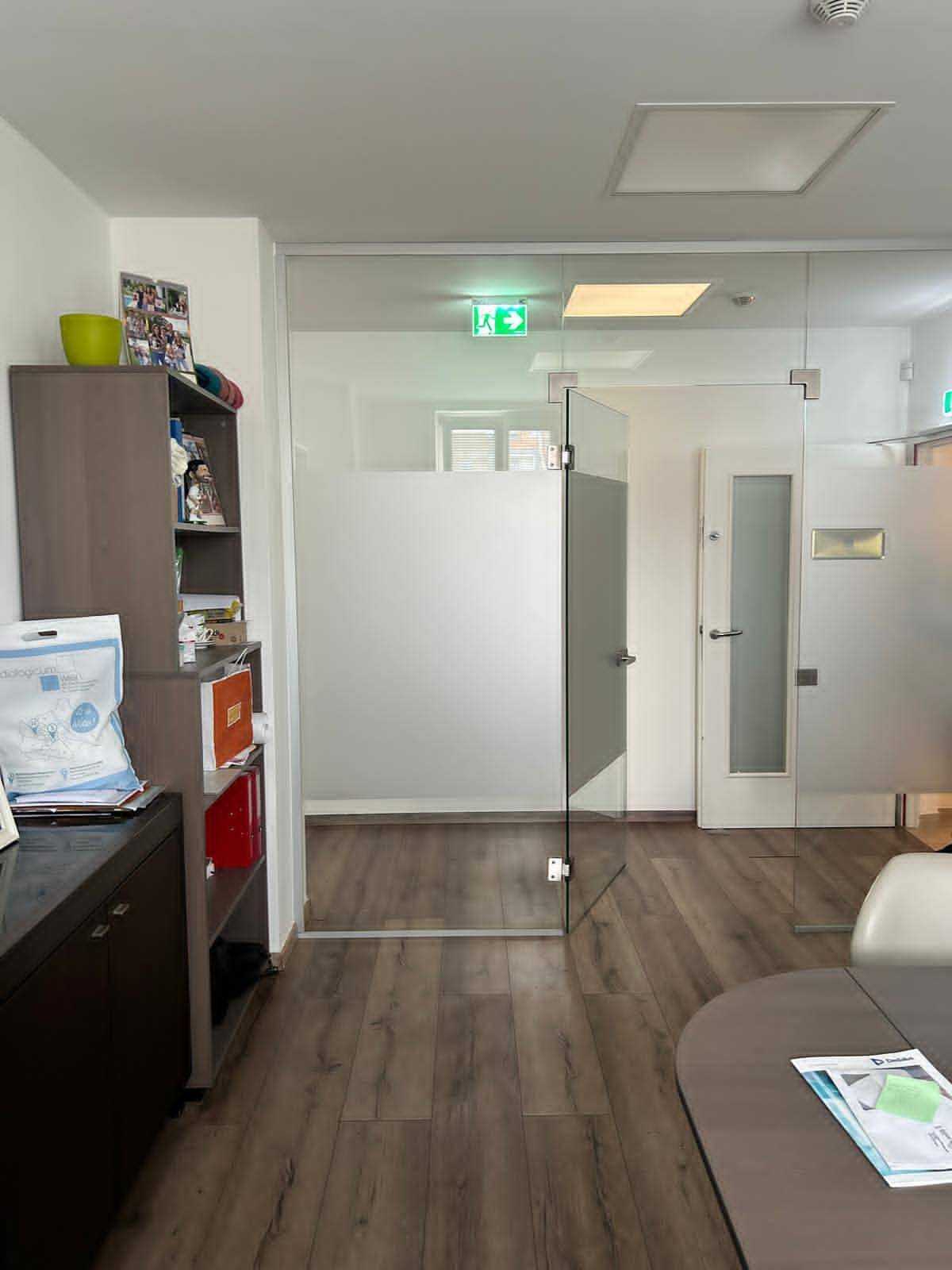 Bürobereich mit einer Glastür, die zu weiteren Räumen führt, und modernem Laminatboden.