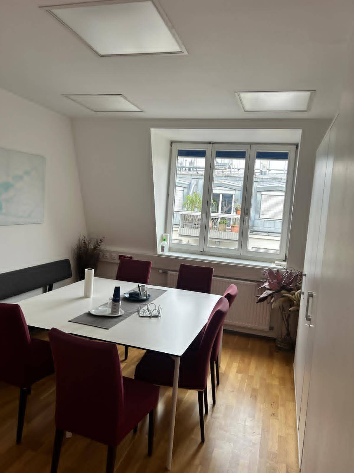 Besprechungsraum mit einem großen Esstisch, roten Stühlen und einem Fenster mit Blick auf eine Terrasse.