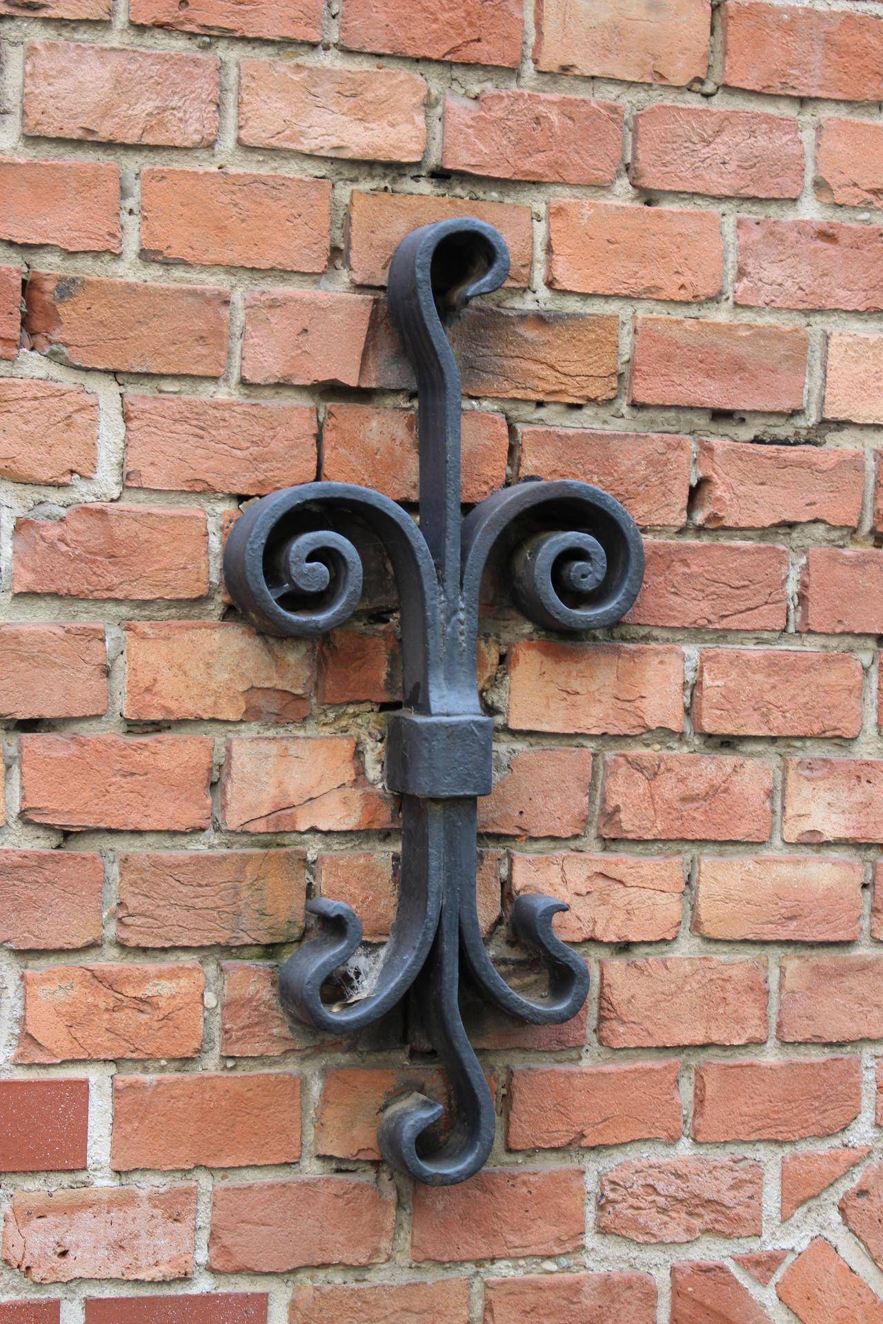 Dekoratives schmiedeeisernes Element an einer Backsteinwand des historischen Gebäudes.