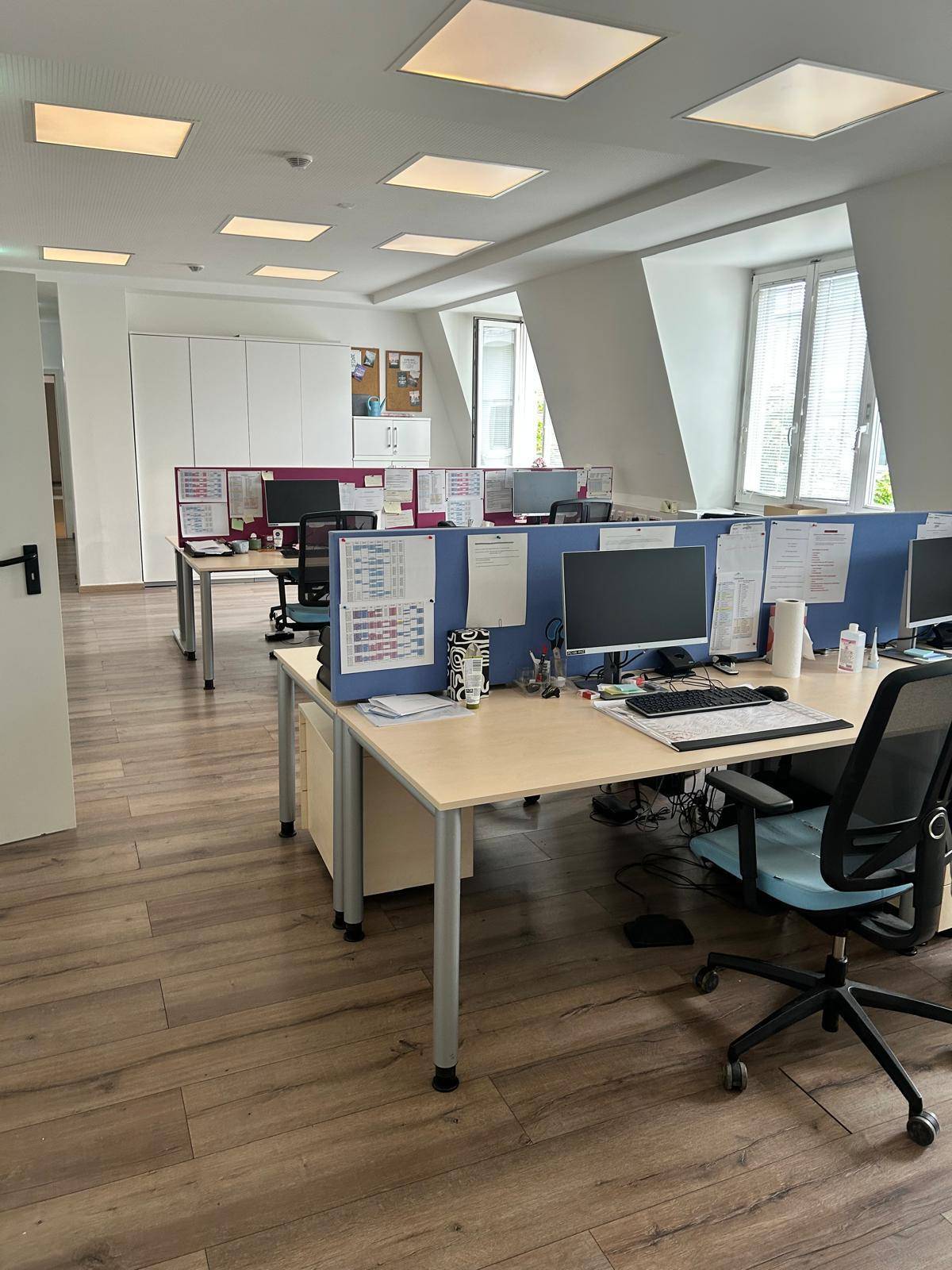 Großraumbüro mit mehreren Arbeitsplätzen, Trennwänden und modernem Laminatboden.