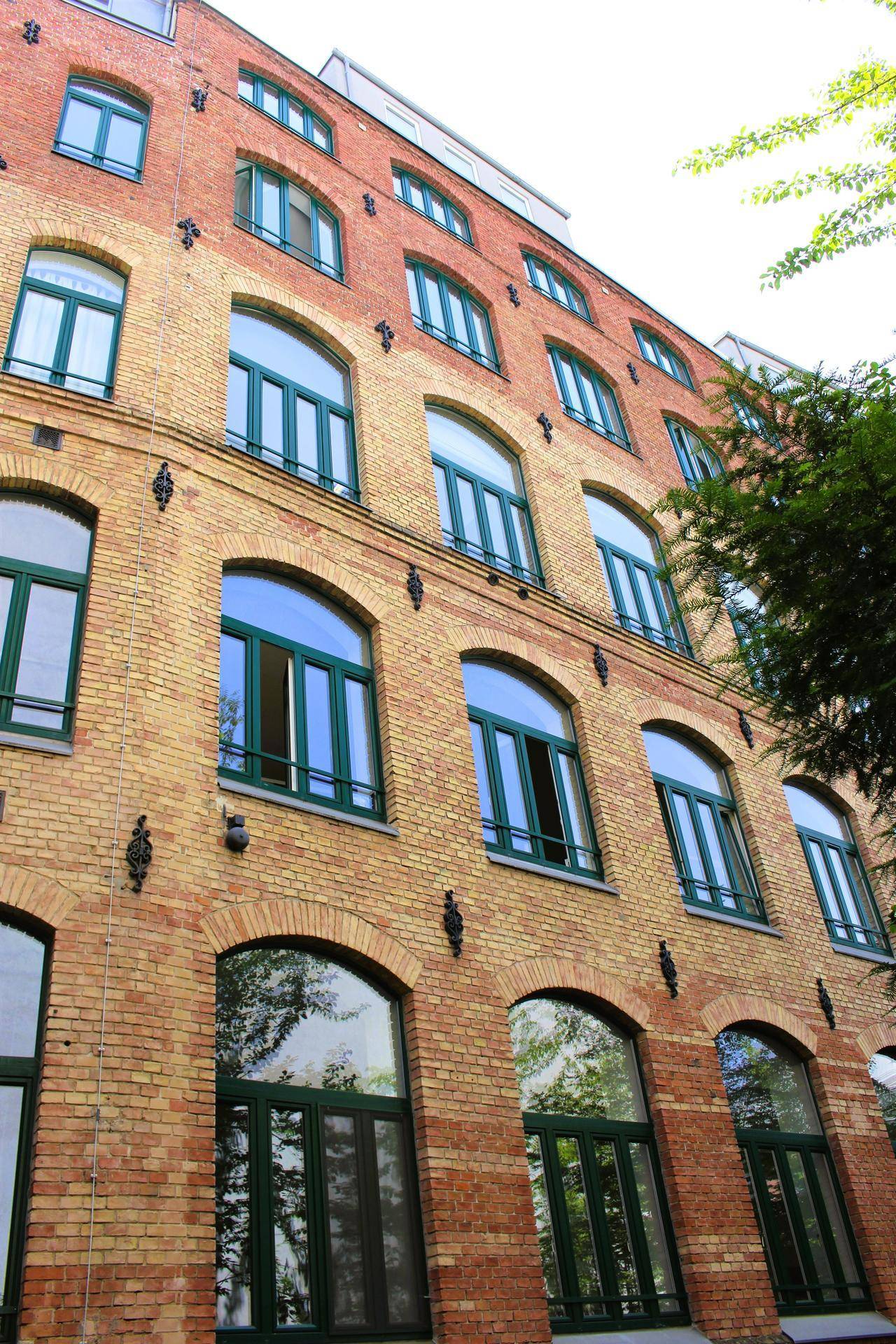 Detailansicht eines historischen Backsteingebäudes mit grünen Fensterrahmen und vielen Bogenfenstern.