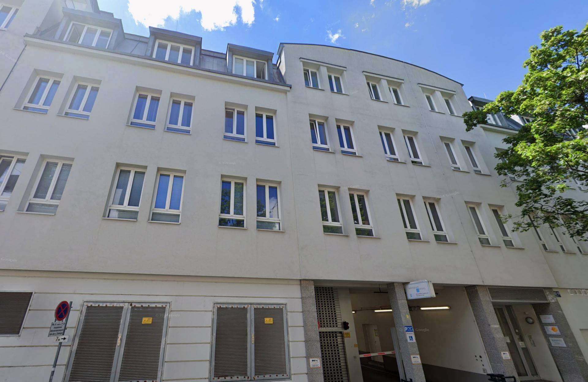 Ansicht der Gebäudefassade mit vielen Fenstern und einem Eingang zu einer Tiefgarage.