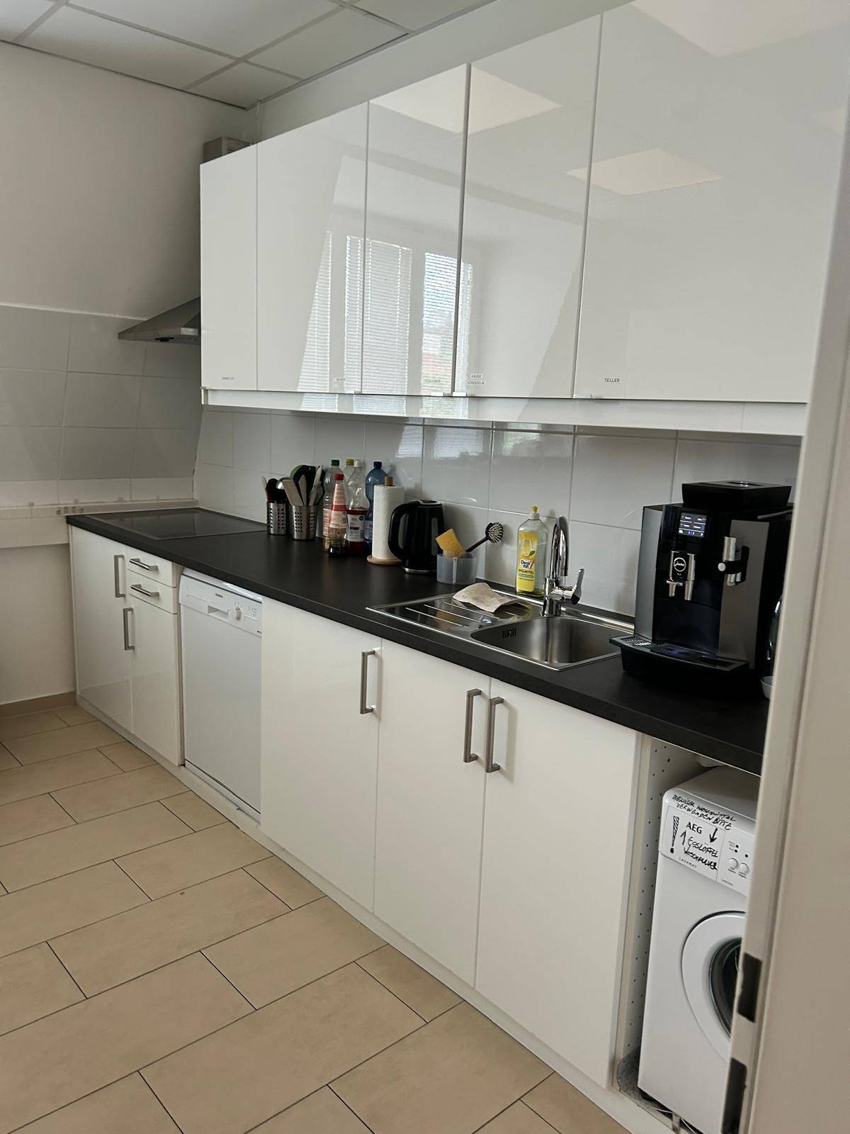 Moderne Büroküche mit glänzenden weißen Schränken, Spülmaschine und Waschmaschine.
