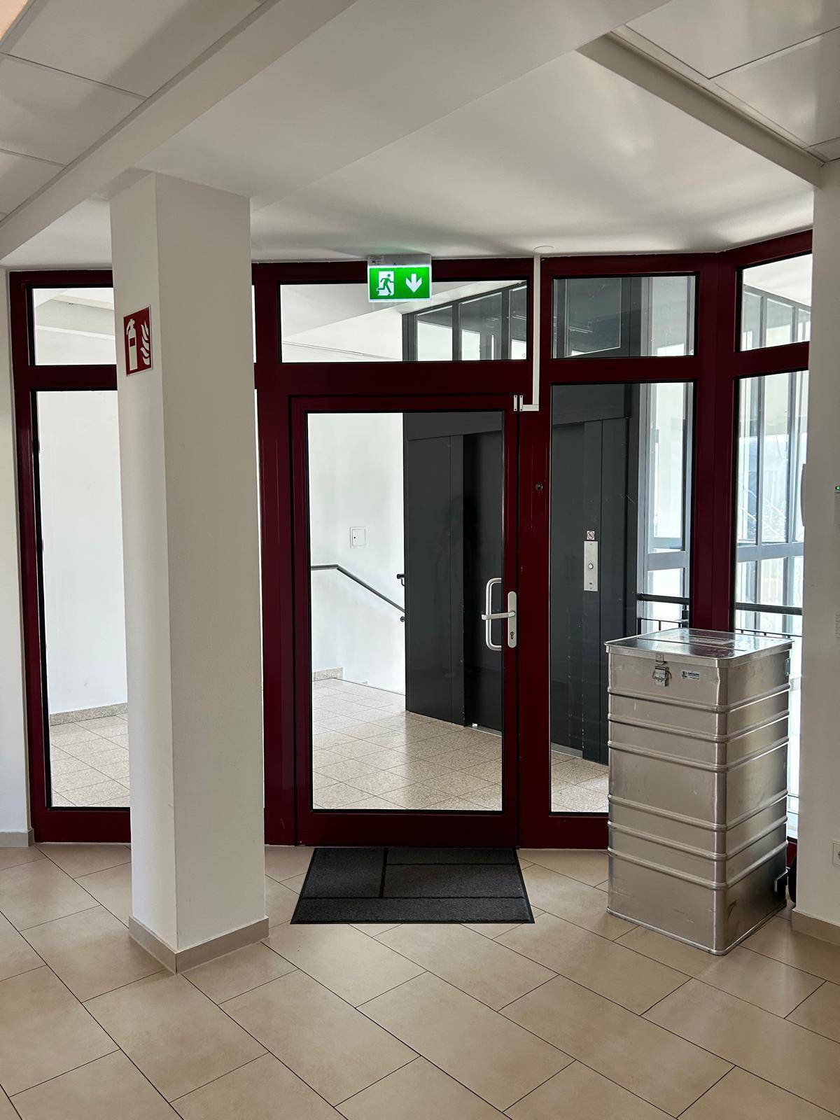 Eingangsbereich eines Bürogebäudes mit großen Glastüren und einem Aufzug im Hintergrund.