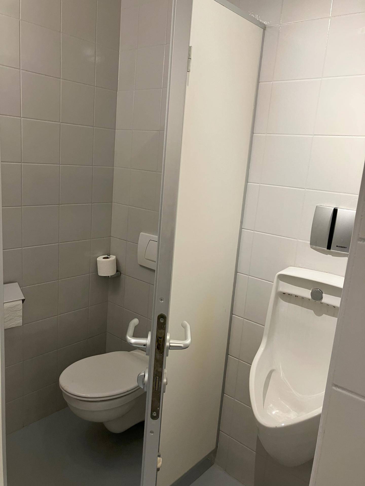 Heller Toilettenraum mit WC und Urinal, hell gefliest und funktional eingerichtet für den täglichen Gebrauch.