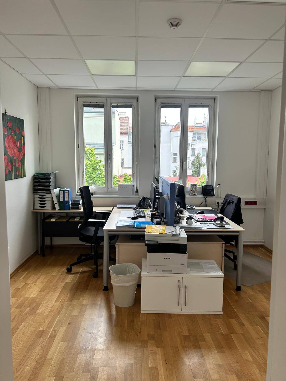 Helles Büro mit zwei Arbeitsplätzen, Holzfußboden und Blick auf die umliegenden Gebäude.