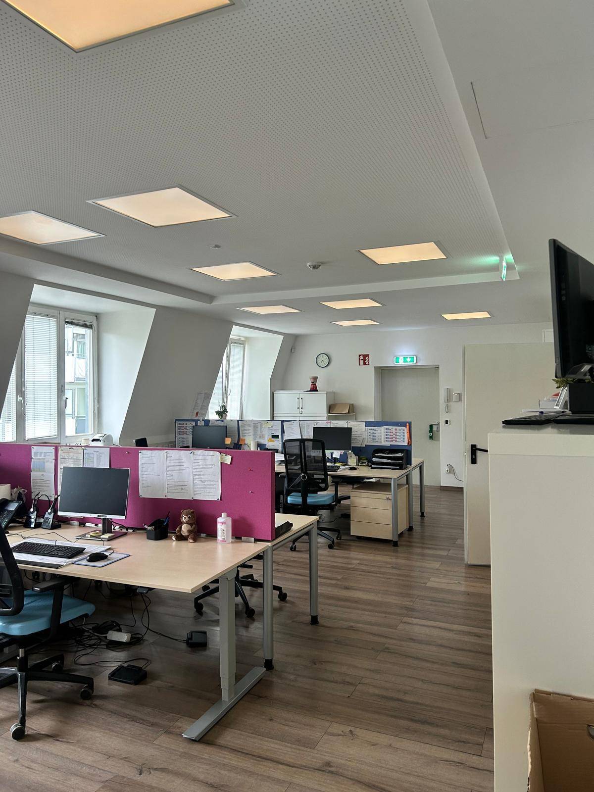 Weitläufiges Großraumbüro mit vielen Arbeitsplätzen, Trennwänden und Deckenbeleuchtung.