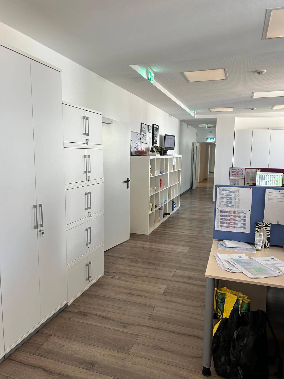 Langer Flur in einem Bürogebäude mit weißen Schränken und Laminatboden.