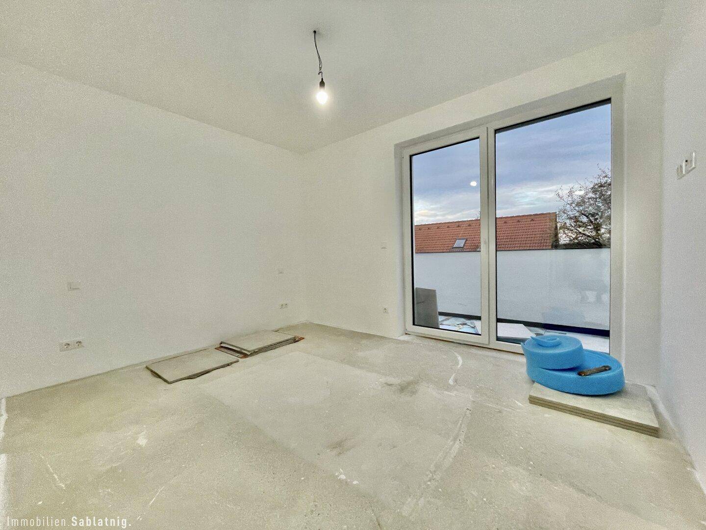 Leeres Schlafzimmer mit großem Fenster und Zugang zu einem Außenbereich, noch im Rohbau.
